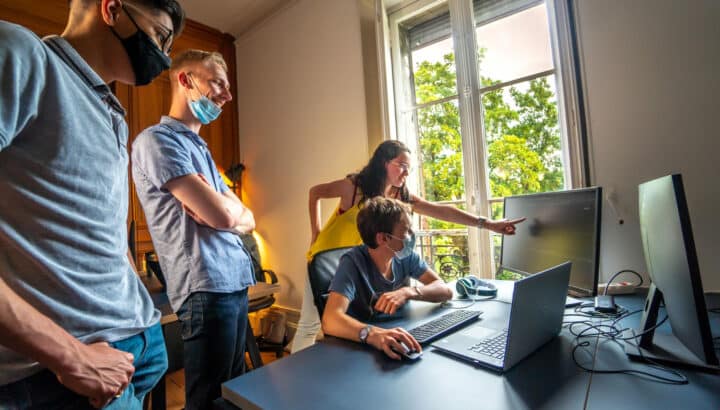 Quatre collègues portant un masque regardant un écran d'ordinateur dans un bureau lumineux