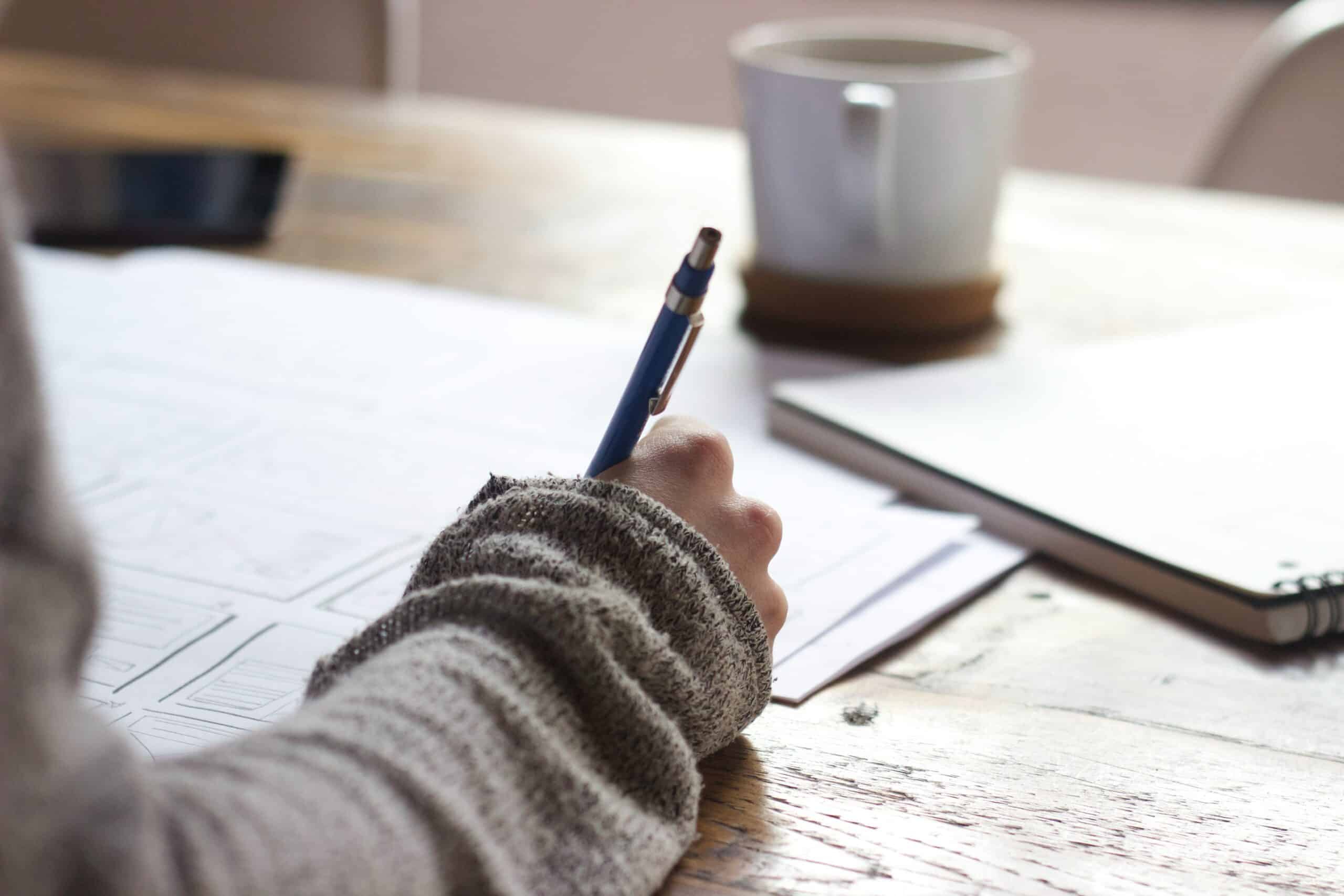 Main dessinant des croquis dans un carnet, tasse de café sur un bureau en bois