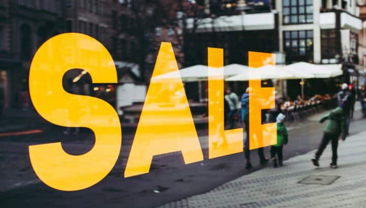 Grand texte orange "SALE" sur une vitrine, rue piétonne en arrière-plan