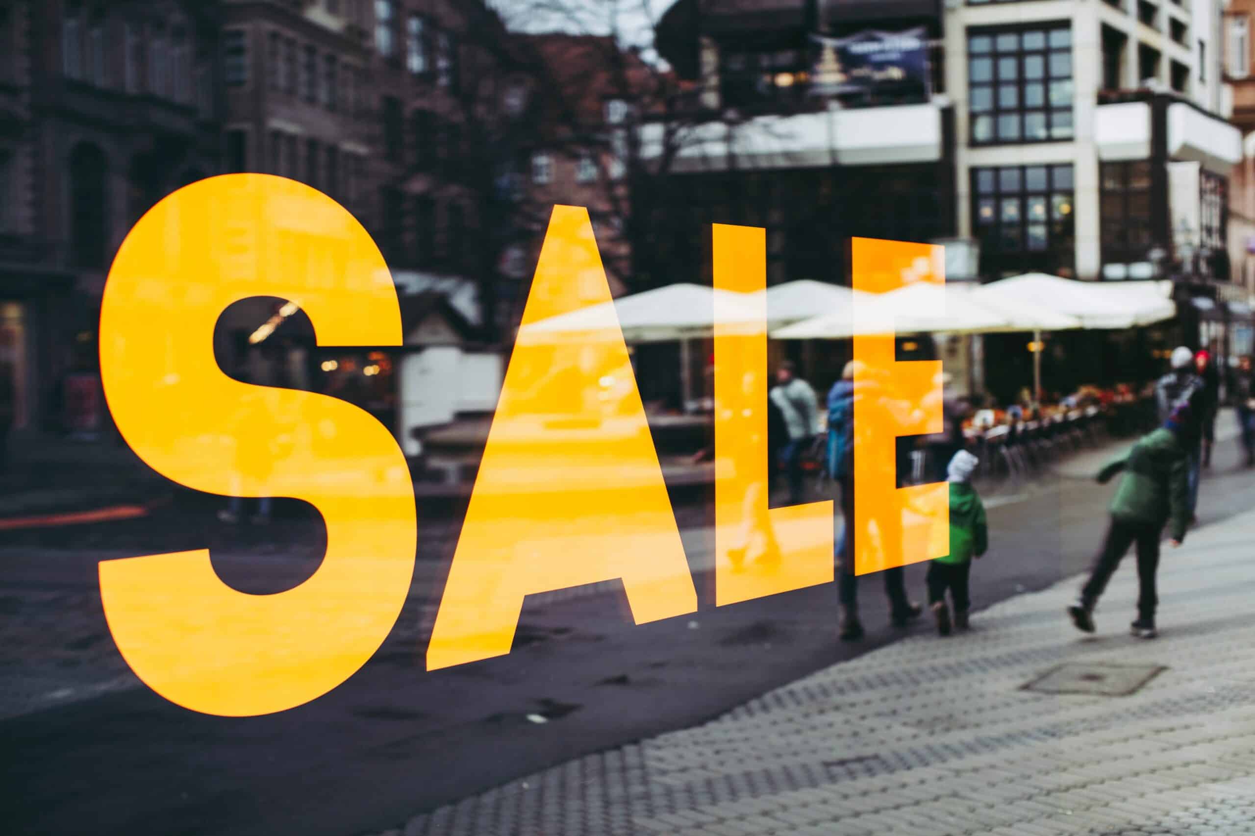 Grand texte orange "SALE" sur une vitrine, rue piétonne en arrière-plan