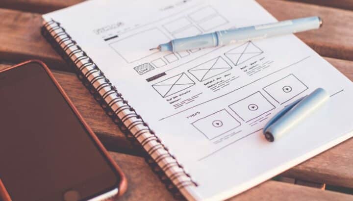 Carnet à spirale avec croquis de wireframes, stylet et smartphone sur une table en bois