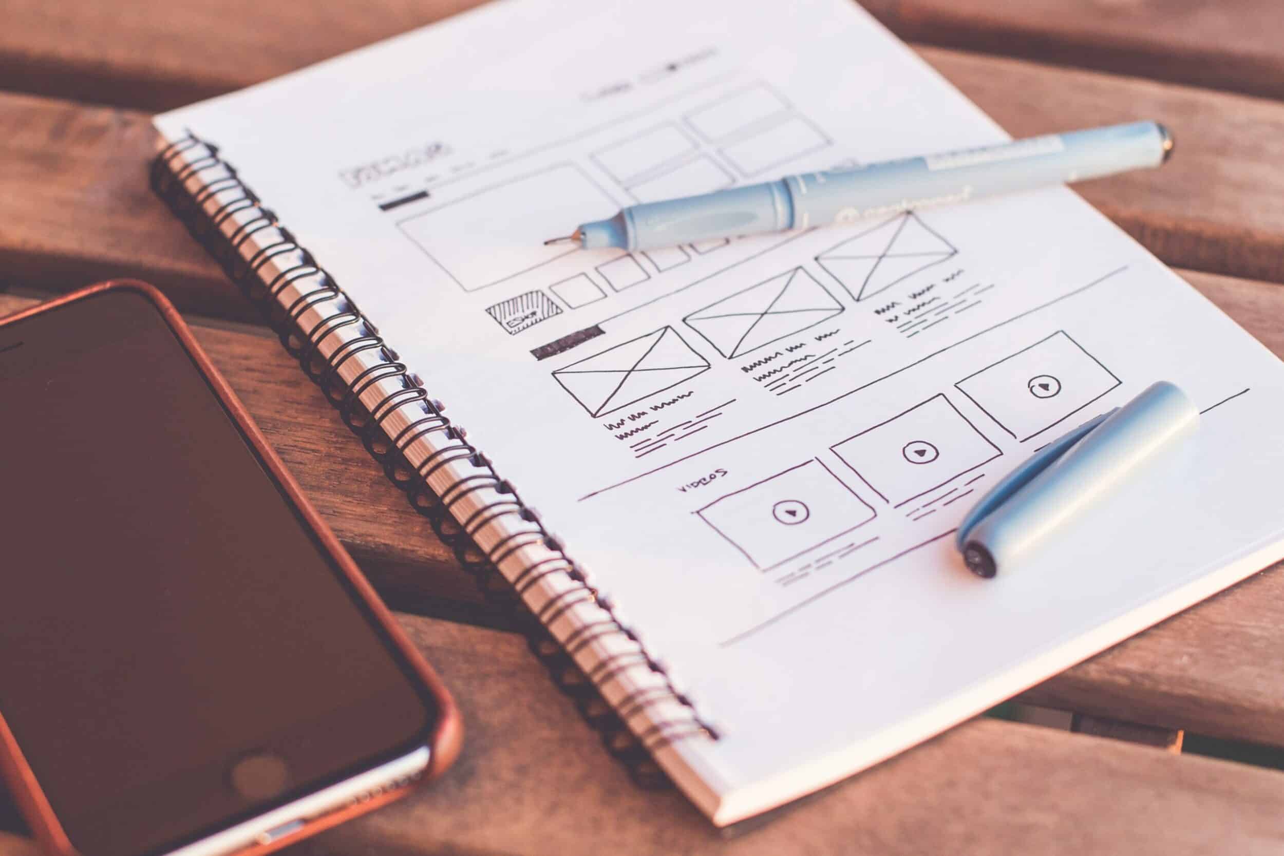 Carnet à spirale avec croquis de wireframes, stylet et smartphone sur une table en bois
