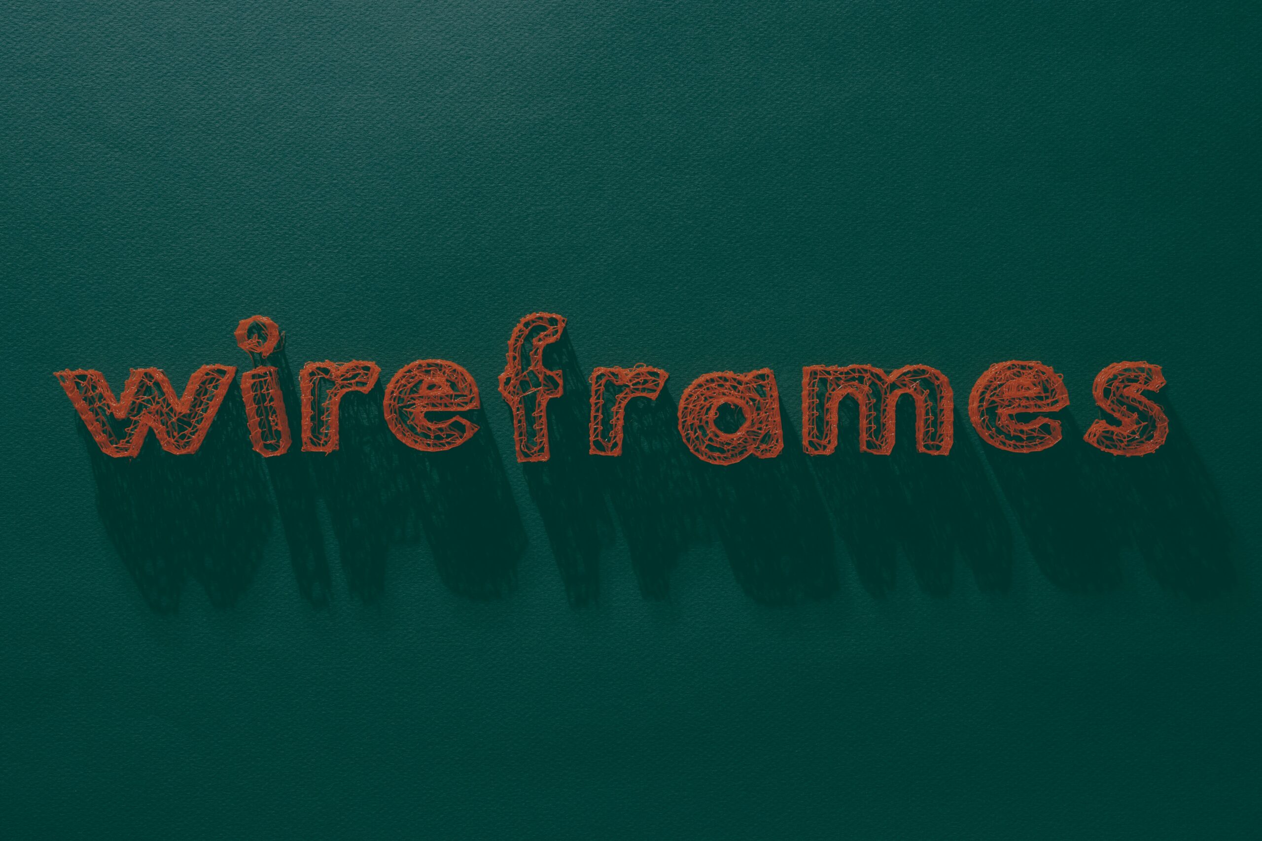 Mot "wireframes" brodé en orange sur un fond de tissu vert texturé