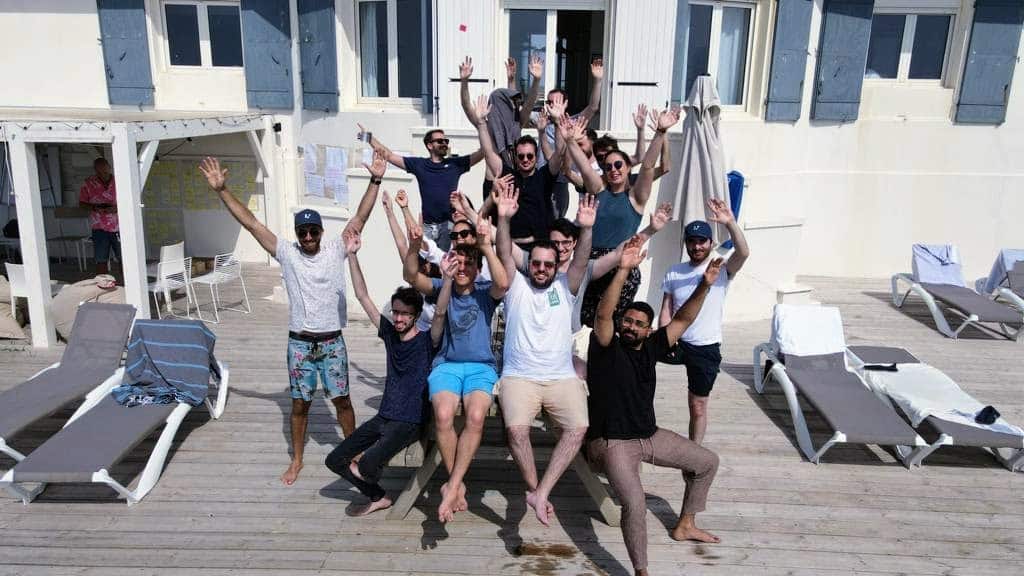 Groupe de collègues sautant et levant les bras sur des transats au bord de la mer