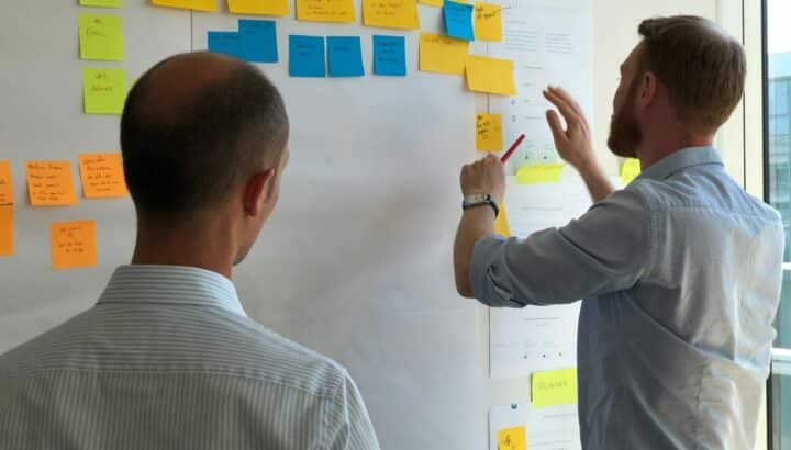 Deux hommes disposant des post-it colorés sur un mur lors d'un atelier collaboratif
