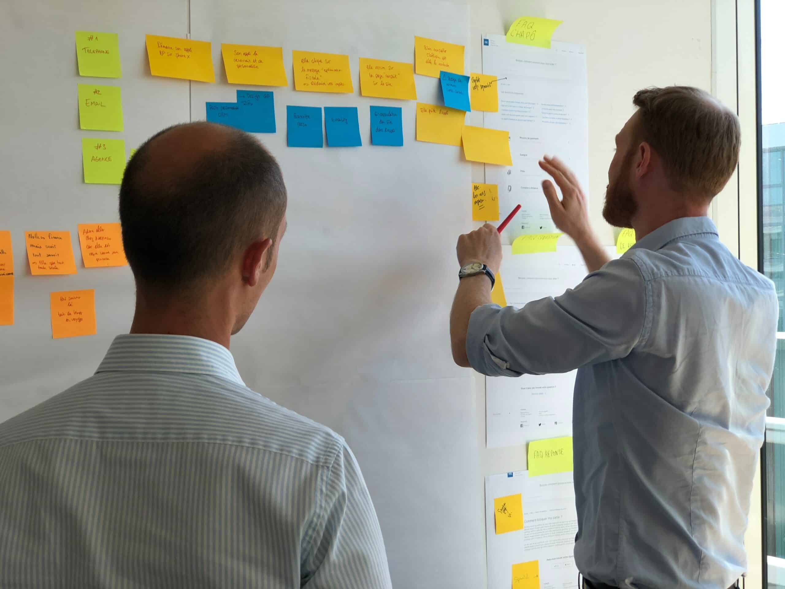 Deux hommes disposant des post-it colorés sur un mur lors d'un atelier collaboratif