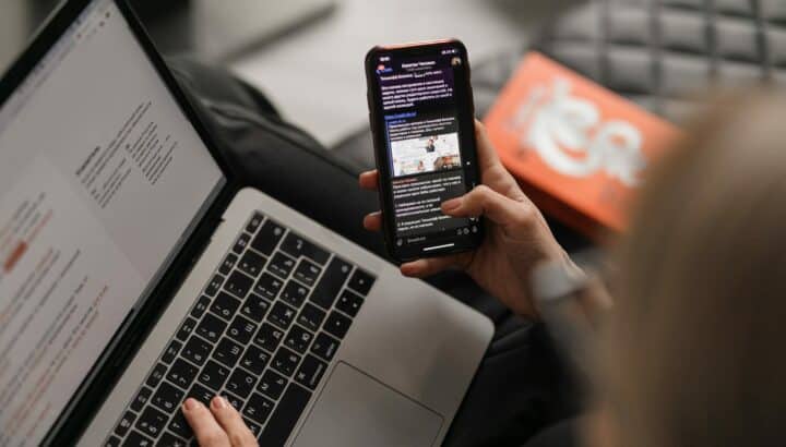 Mains tapant sur un ordinateur portable pendant qu'un smartphone affiche un réseau social