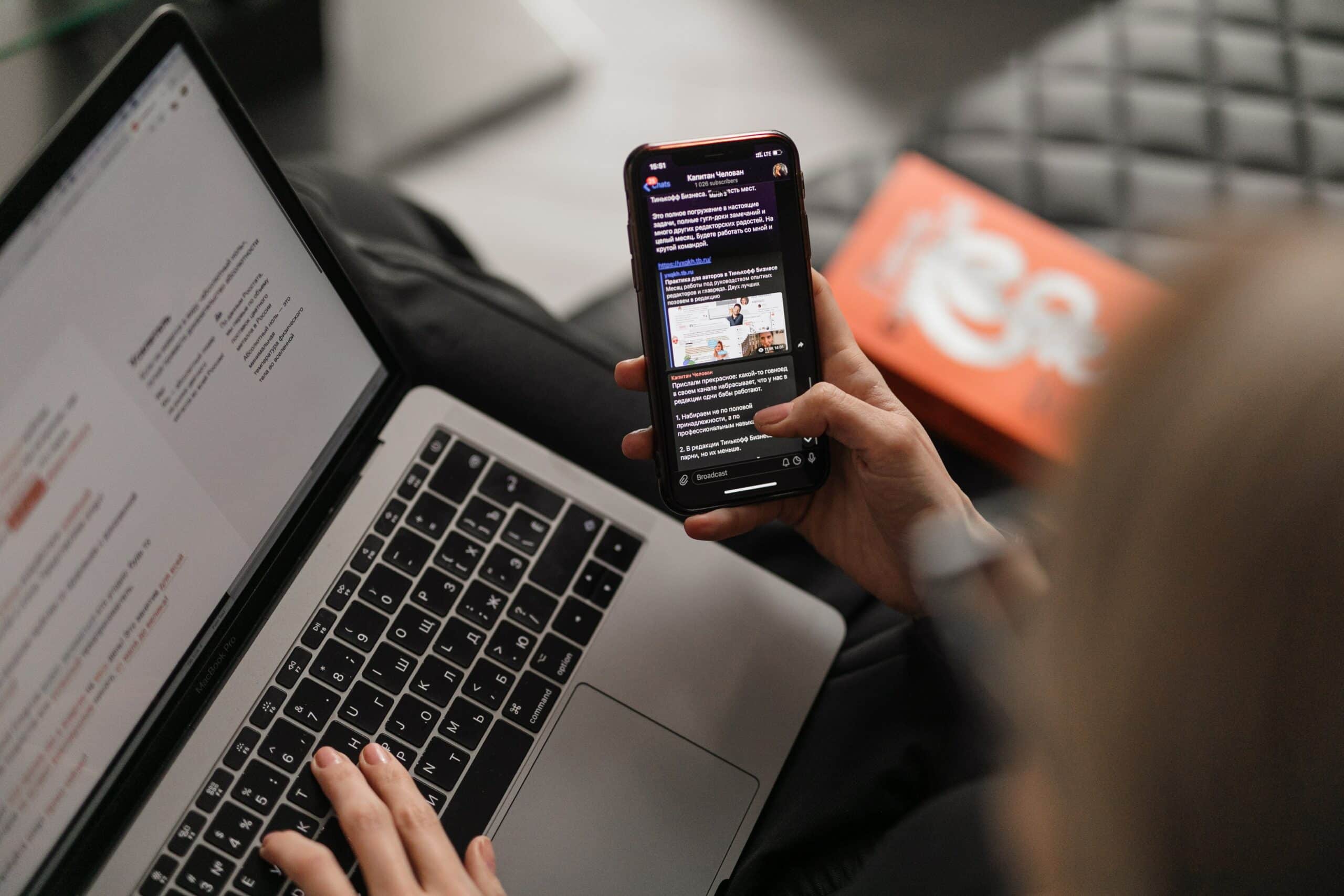 Mains tapant sur un ordinateur portable pendant qu'un smartphone affiche un réseau social