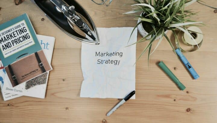 Papier froissé "Marketing Strategy" entouré d'un livre de design et d'une plante, sur bureau en bois