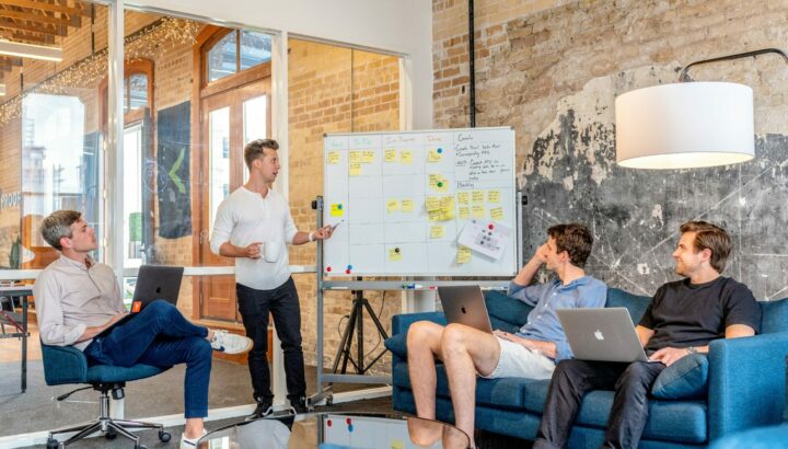 Quatre collègues en réunion dans un bureau loft avec tableau kanban et canapés bleus
