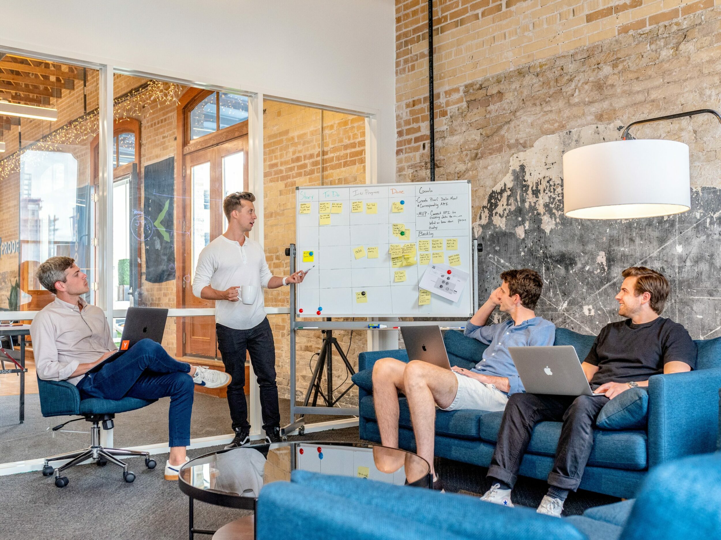 Quatre collègues en réunion dans un bureau loft avec tableau kanban et canapés bleus