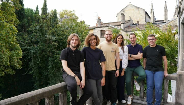 Six collègues posant sur un balcon avec vue sur les toits de Bordeaux