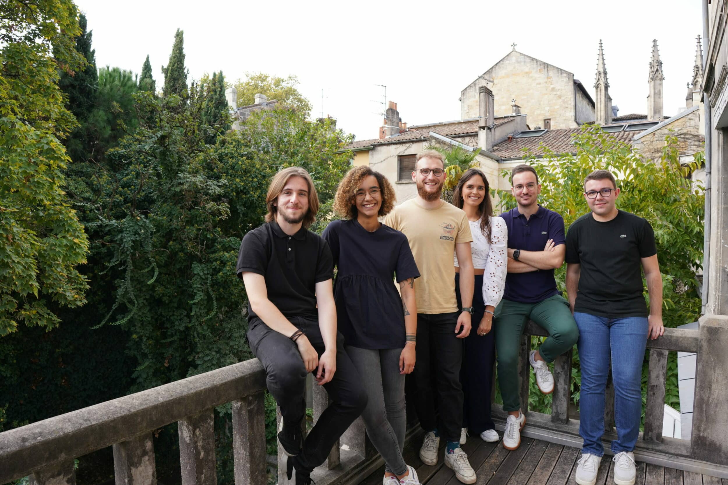 Six collègues posant sur un balcon avec vue sur les toits de Bordeaux