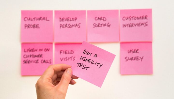 Main tenant un post-it "Run a usability test" devant d'autres post-it de méthodes UX