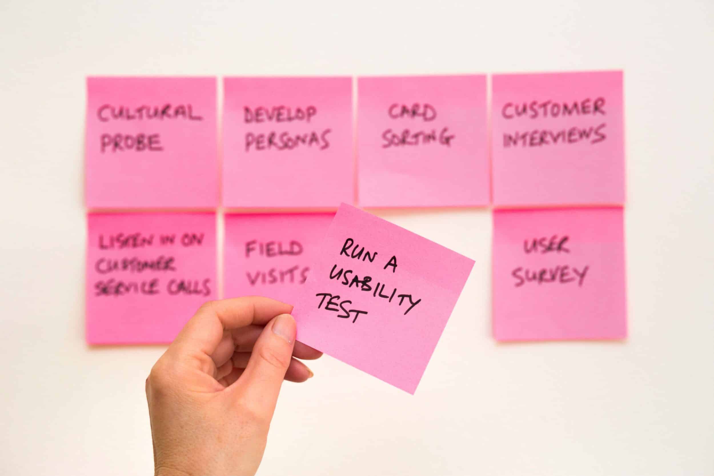 Main tenant un post-it "Run a usability test" devant d'autres post-it de méthodes UX