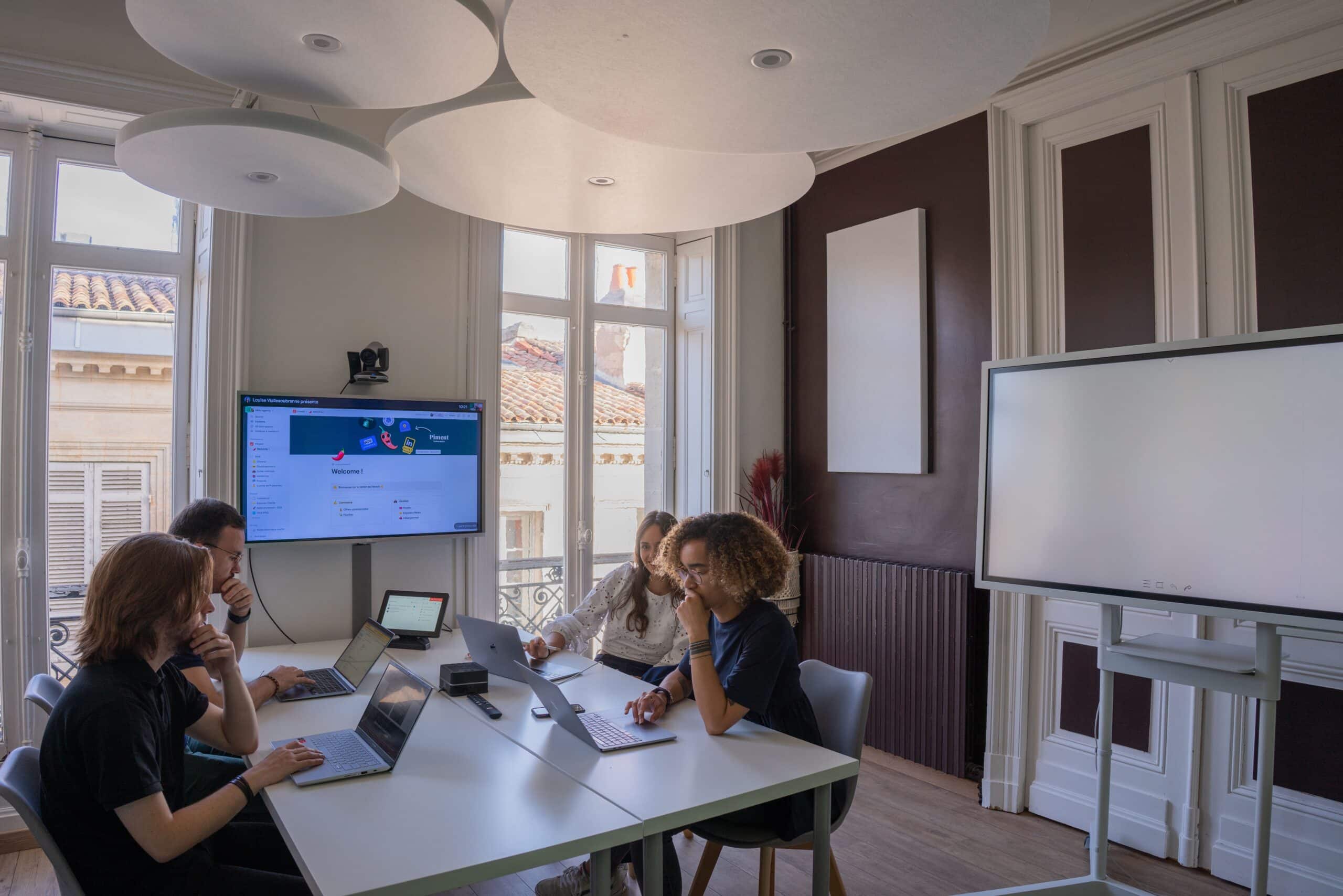Quatre personnes en réunion dans une salle avec écrans connectés et tableau interactif