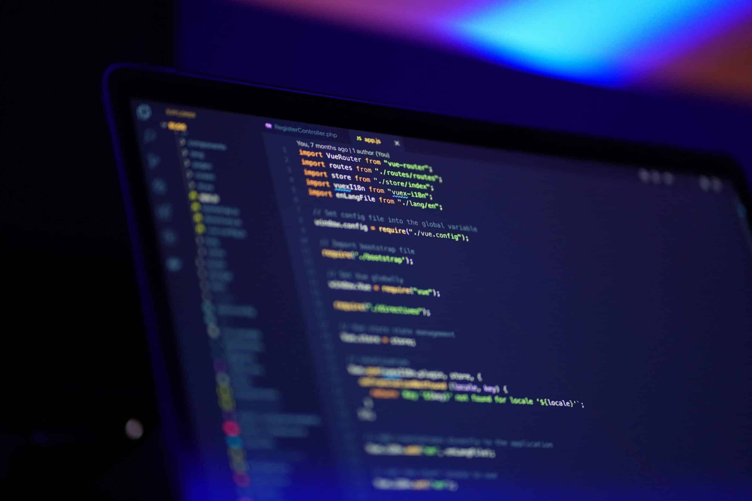 Écran de laptop affichant du code Vue.js, éclairage bokeh coloré en arrière-plan
