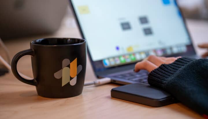 Tasse et téléphone avec logo Mink posés sur un bureau, ordinateur portable flouté en arrière-plan