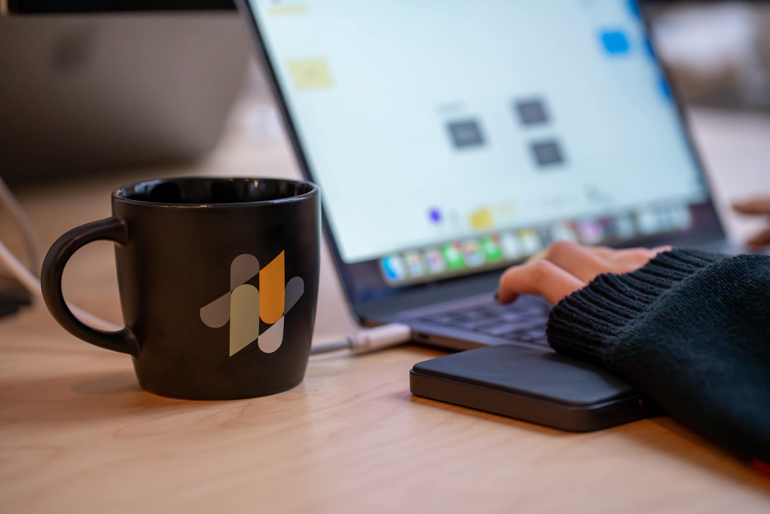 Tasse et téléphone avec logo Mink posés sur un bureau, ordinateur portable flouté en arrière-plan