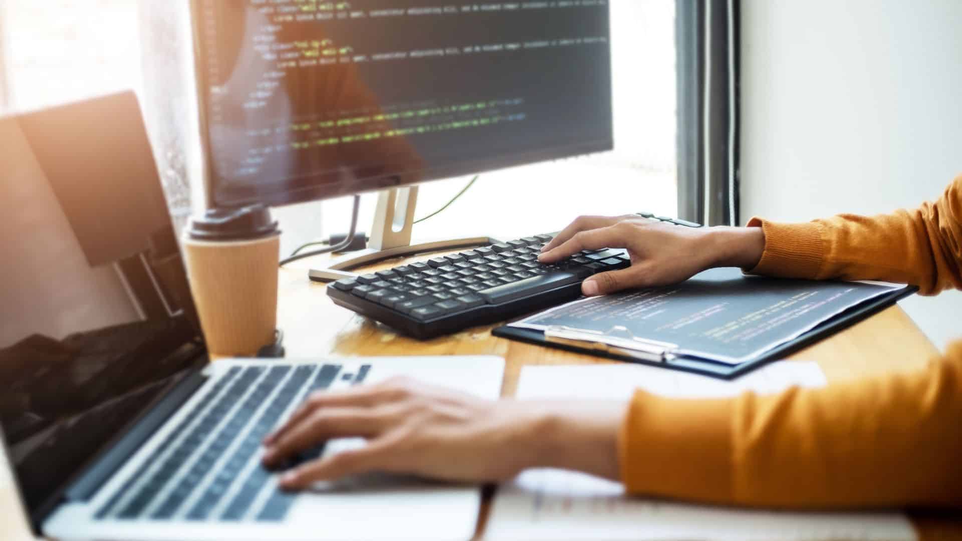 Mains tapant sur deux claviers, écrans de code en arrière-plan, tasse de café