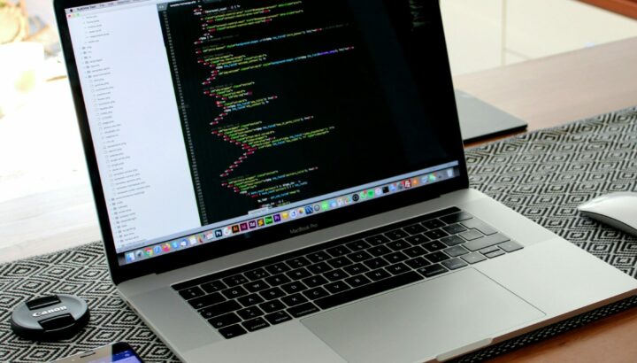 MacBook Pro affichant du code, bouchon d'objectif Canon et smartphone à côté