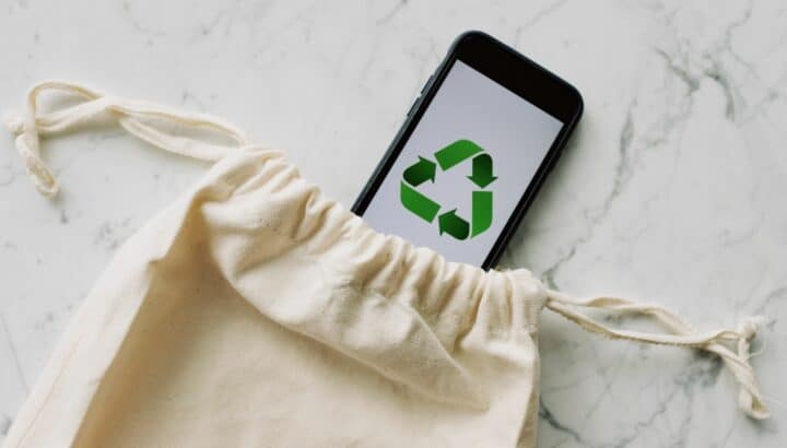 Smartphone affichant un symbole de recyclage vert, posé dans un sac en tissu sur fond marbré