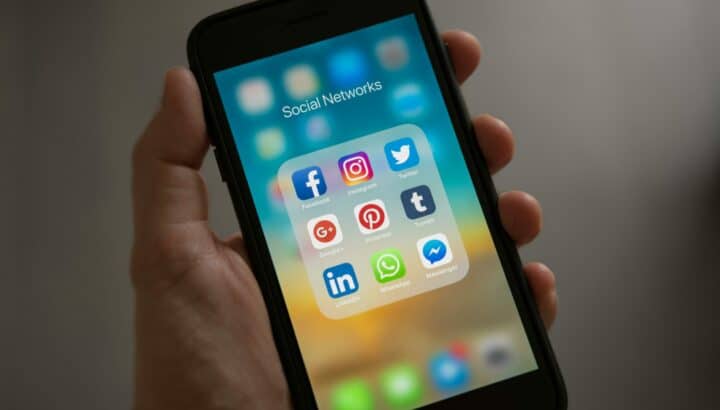 Main tenant un smartphone avec un dossier d'applications intitulé "Social Networks" (Facebook, Instagram, Twitter, etc.)