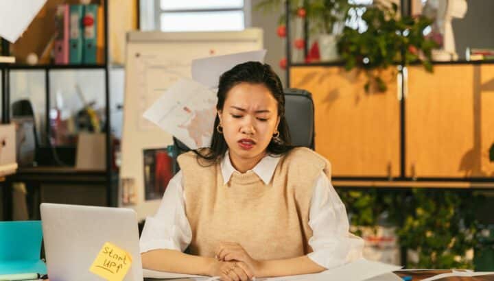 Femme à son bureau, main sur ordinateur portable, note autocollante "Start Up", air soucieux
