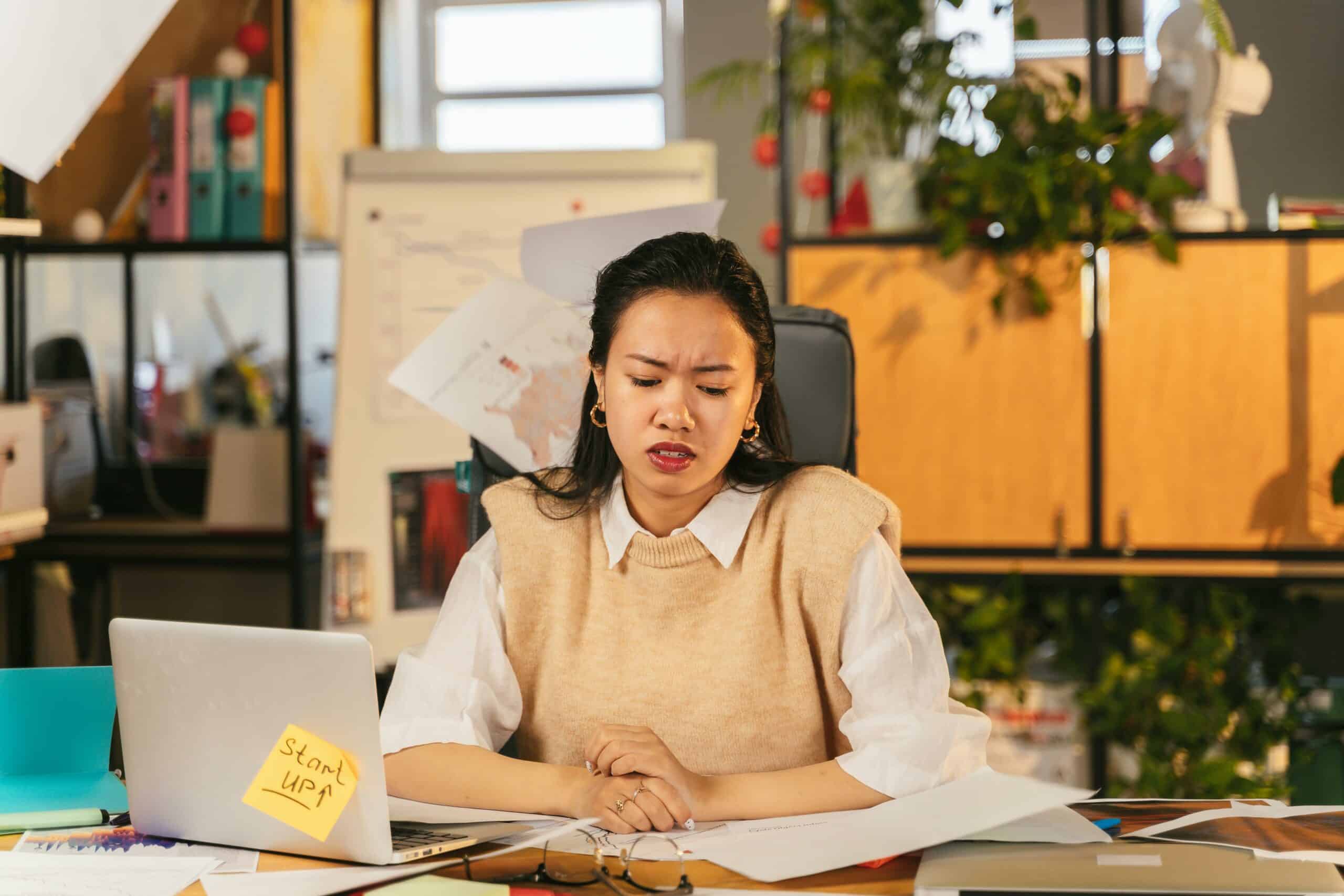 Femme à son bureau, main sur ordinateur portable, note autocollante "Start Up", air soucieux