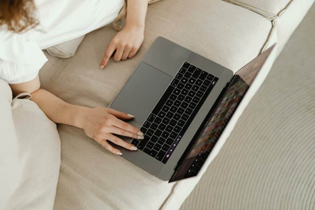 Vue du dessus d'une femme allongée sur un canapé beige tapant sur un ordinateur portable