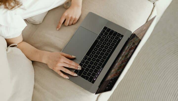 Vue du dessus d'une femme allongée sur un canapé beige tapant sur un ordinateur portable