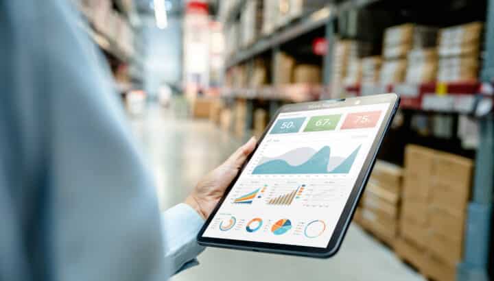 Main tenant une tablette avec graphiques de rapport de magasin, entrepôt logistique en arrière-plan