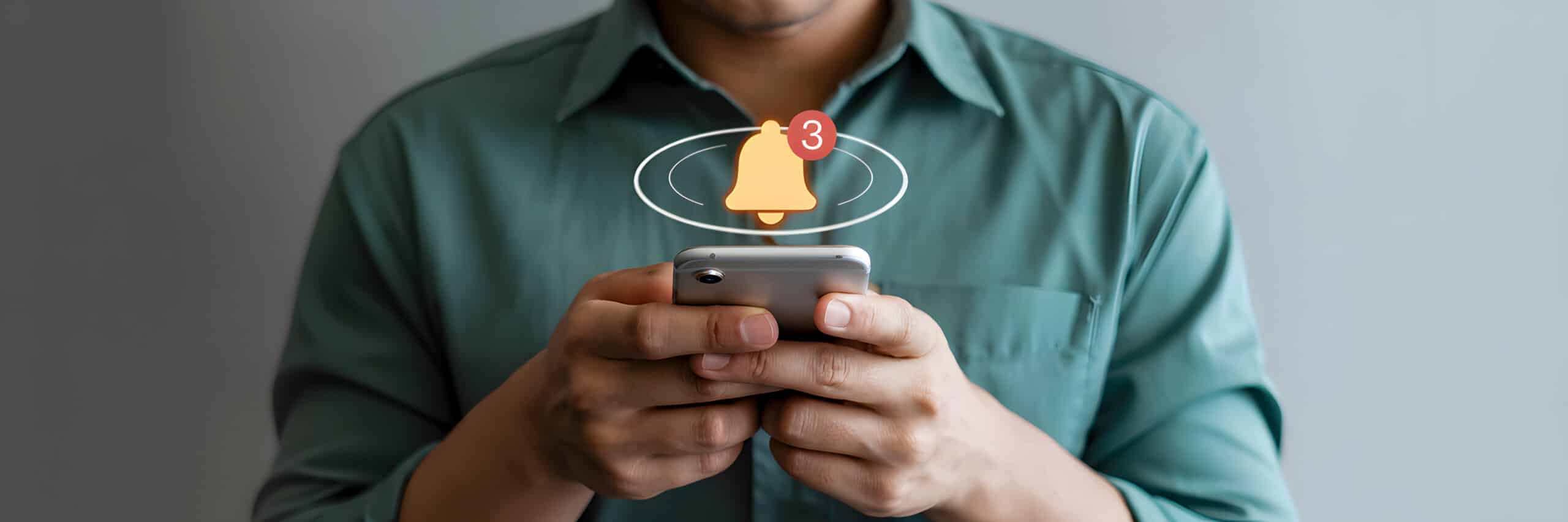 Homme en chemise verte tenant un smartphone, icône de cloche de notification avec le chiffre 3 au-dessus de l'appareil