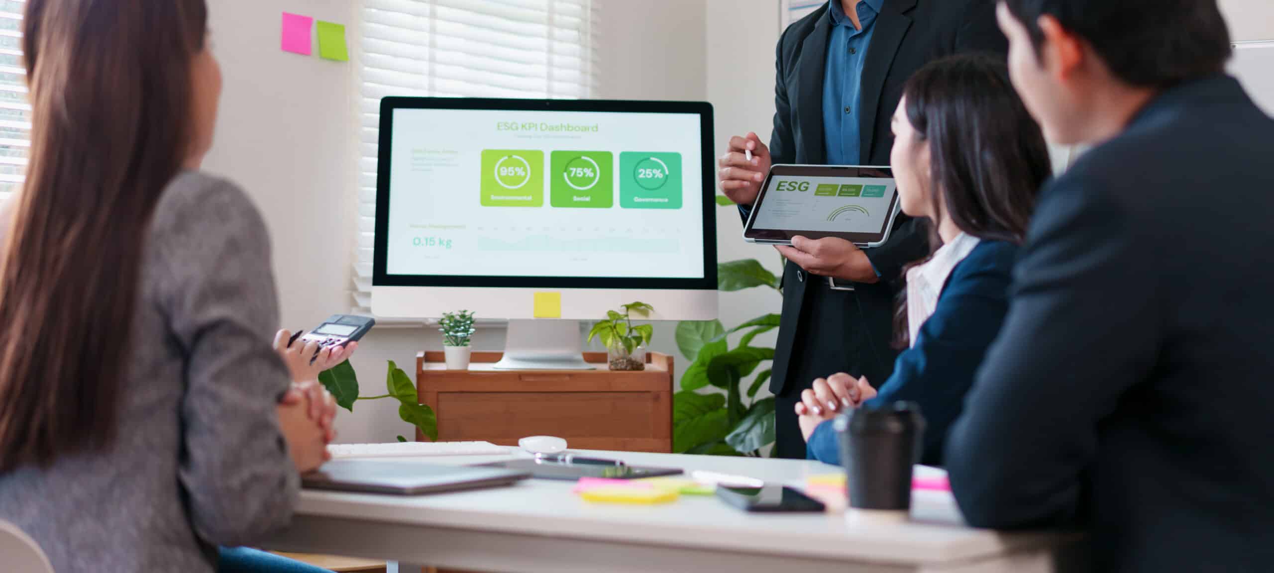 Homme présentant un tableau de bord ESG affichant des indicateurs de gouvernance, environnement et social à trois collègues assis autour d'une table