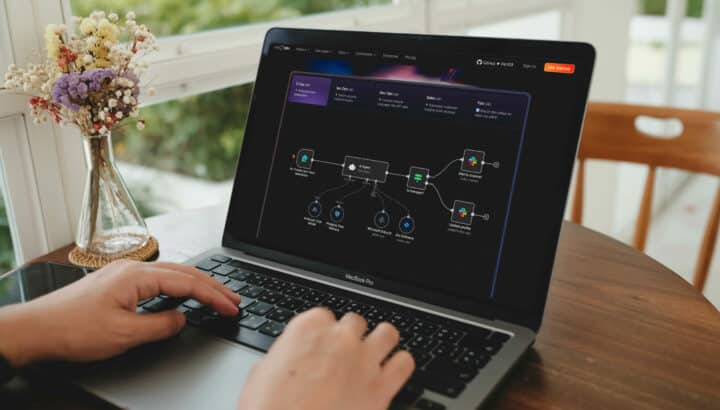 Mains tapant sur un MacBook Pro affichant l'interface du site n8n avec un schéma de workflow d'automatisation impliquant IA, Slack et Jira
