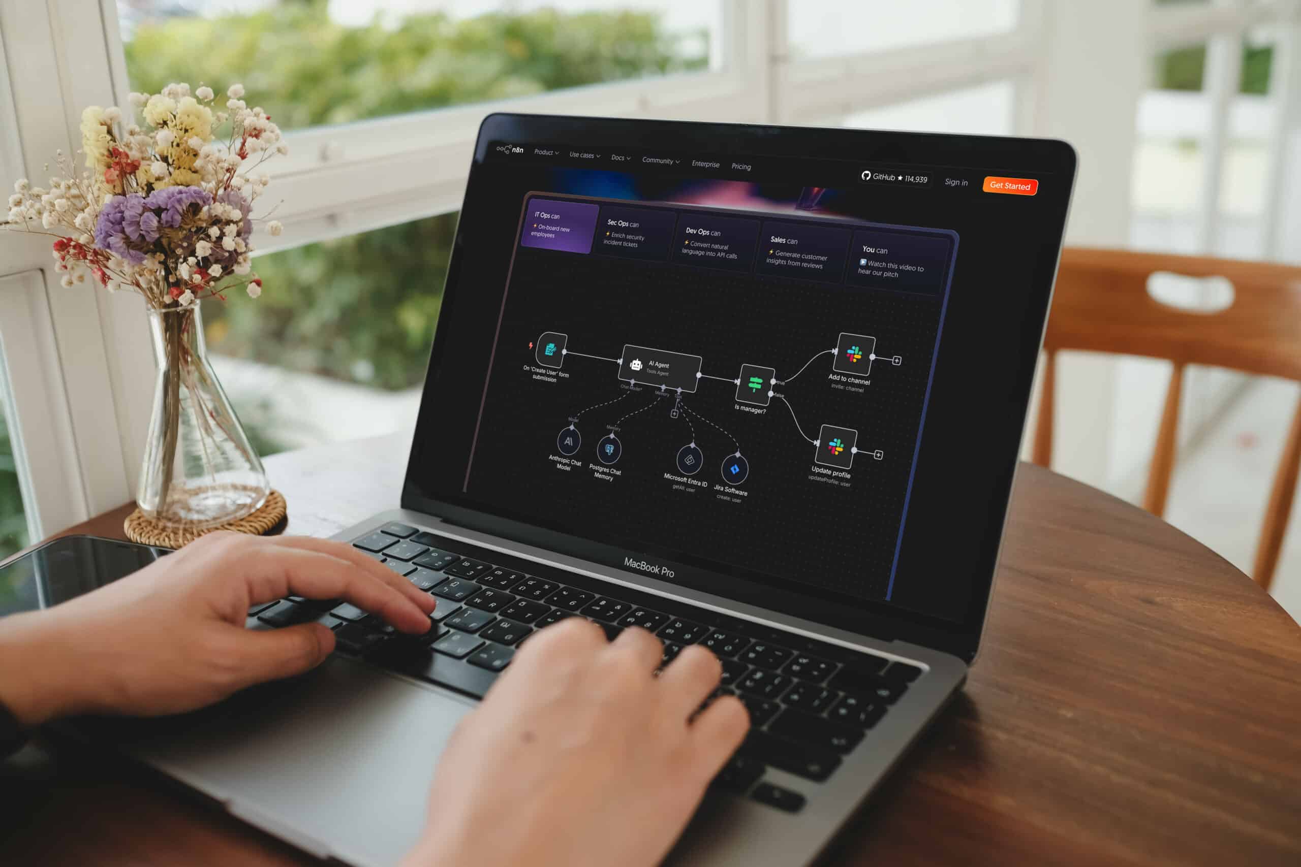 Mains tapant sur un MacBook Pro affichant l'interface du site n8n avec un schéma de workflow d'automatisation impliquant IA, Slack et Jira