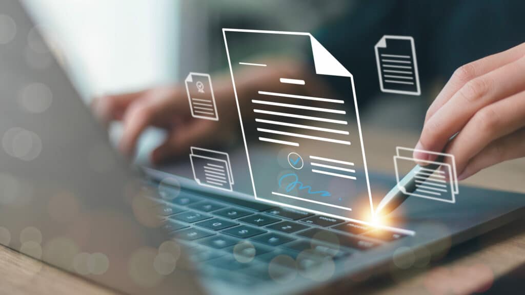 Mains tapant sur un clavier d'ordinateur portable, superposées d'icônes de documents dématérialisés dont un contrat avec signature électronique