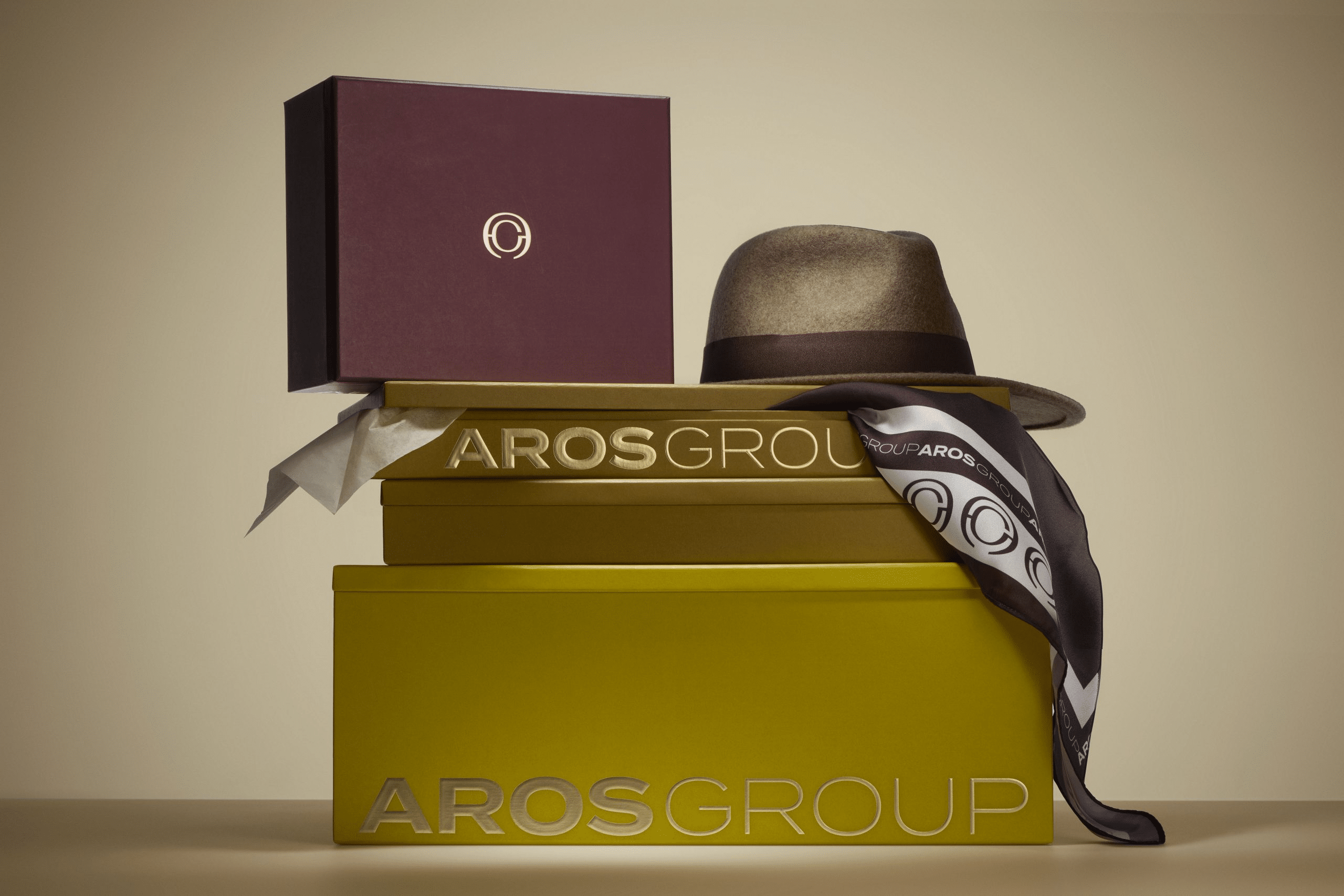 Coffrets de packaging de luxe aux couleurs bordeaux et doré gravés "AROS Group", accompagnés d'un chapeau en feutre et d'un foulard imprimé du logo de la marque