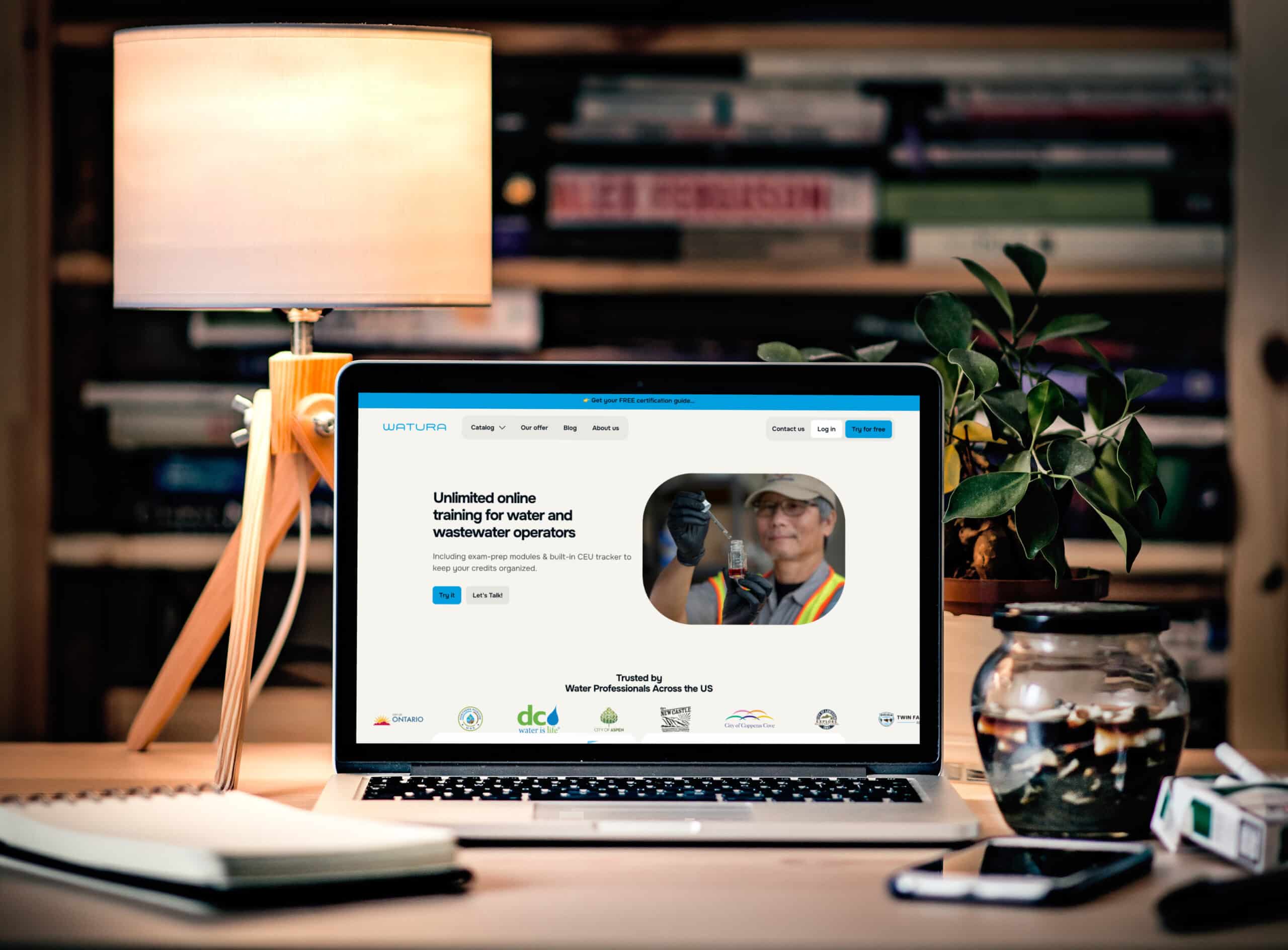 Ordinateur portable affichant le site Watura sur un bureau avec lampe et plante