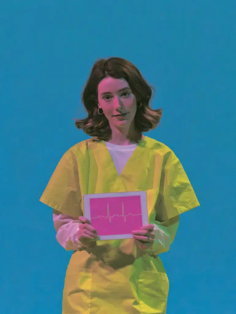 Femme en blouse médicale jaune tenant une tablette affichant un tracé d'électrocardiogramme rose, fond bleu